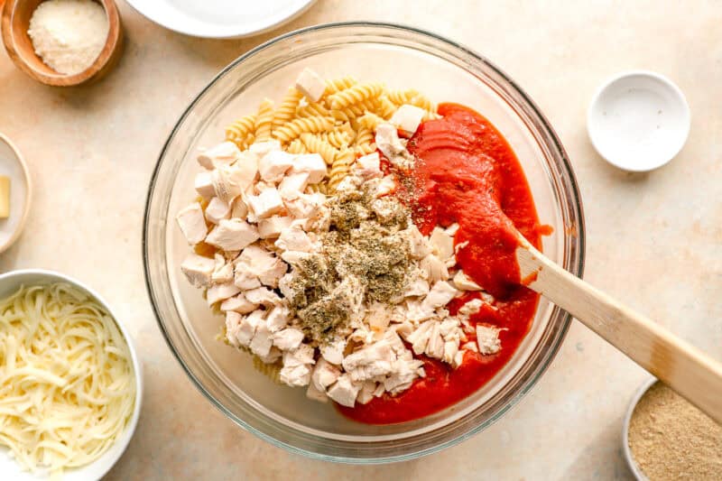 ingredients for chicken parmesan casserole in a bowl with a wooden spoon.