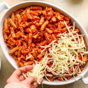 sprinkling shredded mozzarella cheese over chicken parmesan casserole in a baking dish.