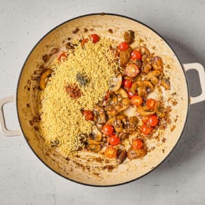 orzo and spices over sautéed vegetables in a pan.