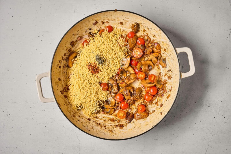 orzo and spices over sautéed vegetables in a pan.