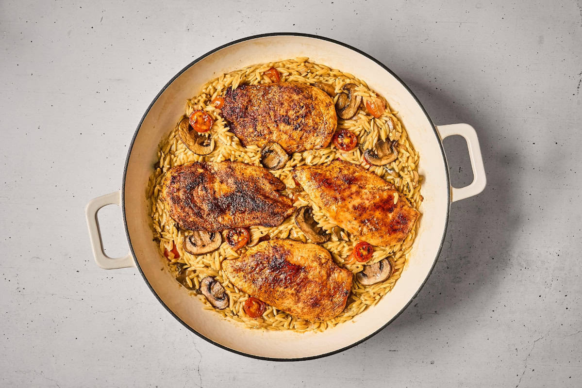 vegetable orzo topped with seared chicken breasts in a pan.