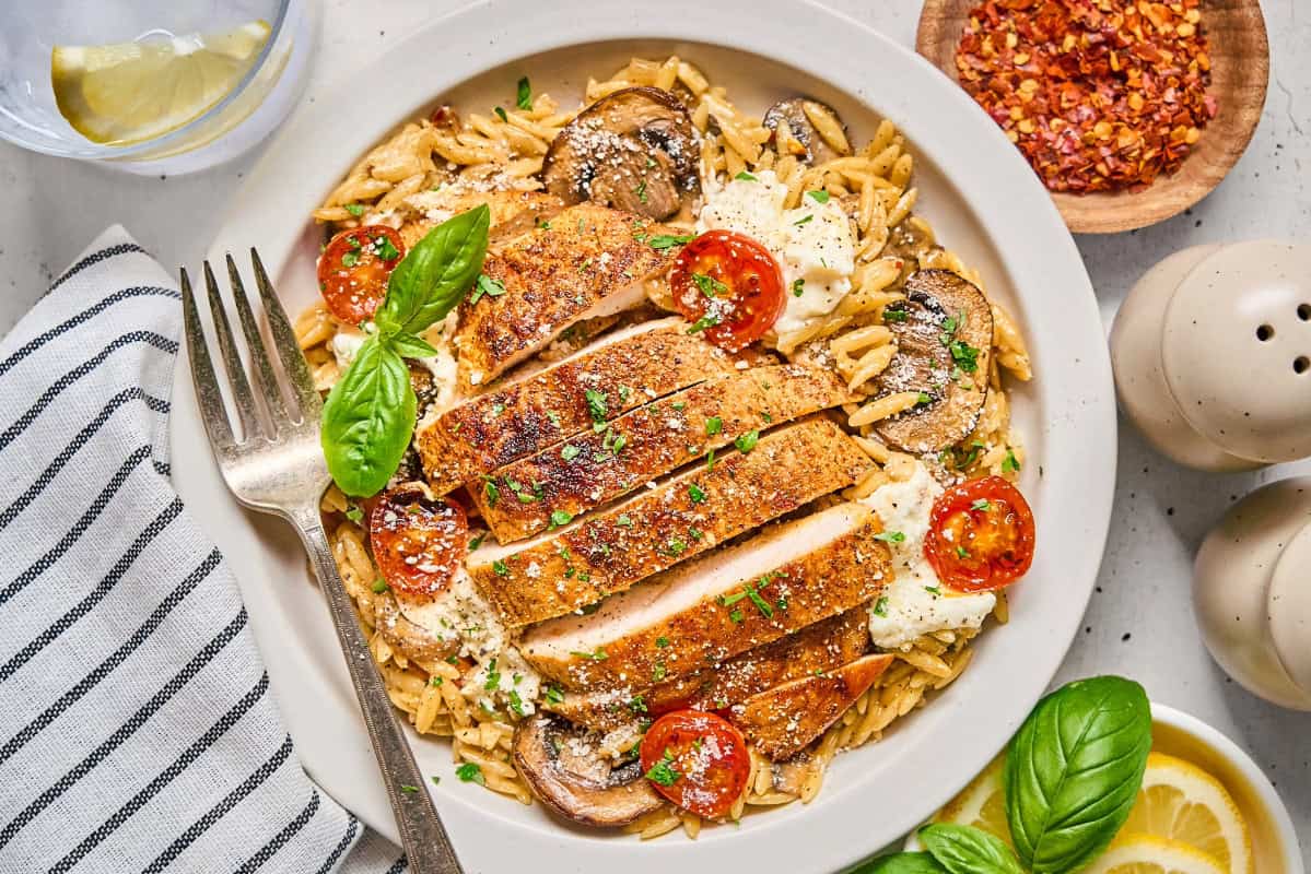 a sliced chicken breast over vegetable orzo and ricotta cheese with a fork.