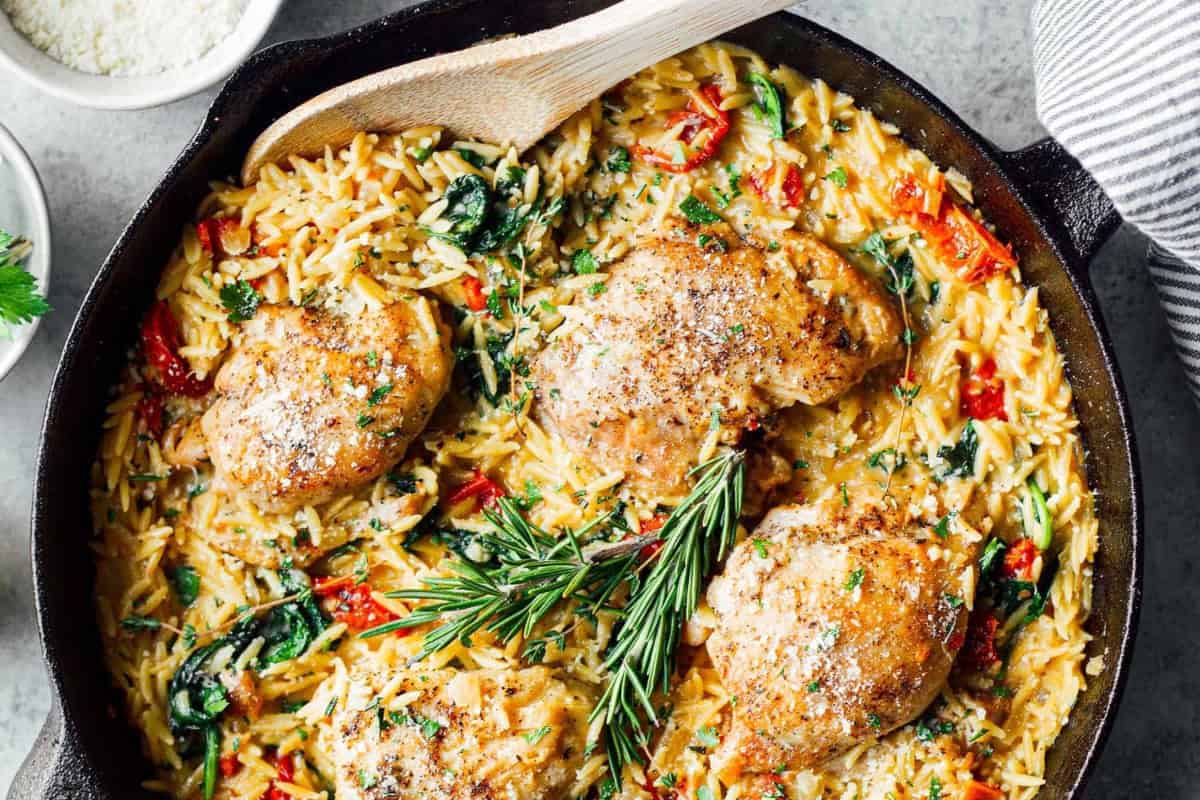 a skillet of tuscan chicken orzo with a wooden serving spoon.