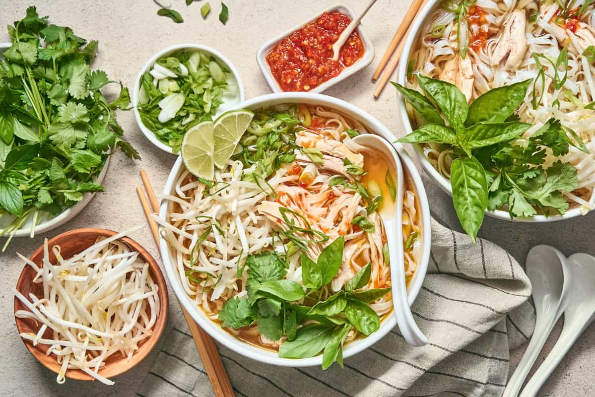 a bowl of chicken pho with a spoon surrounded by toppings.
