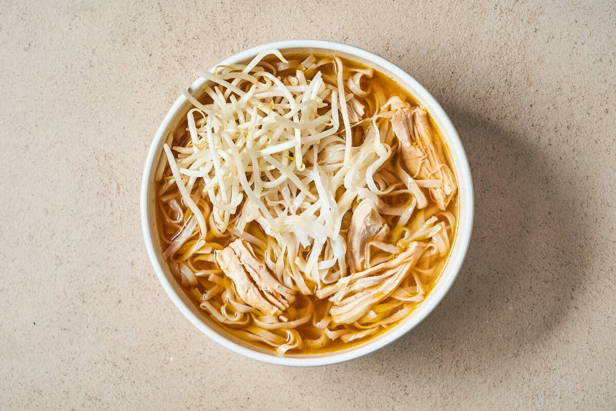 a bowl of pho broth filled with shredded chicken thighs and bean sprouts.
