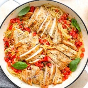 overhead view of bruschetta chicken pasta in a pan with basil leaves and fresh Parmesan.