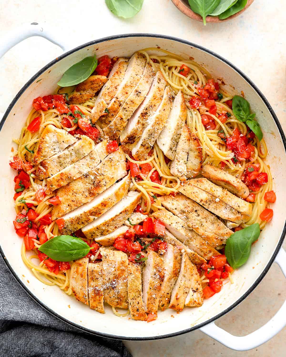 overhead view of bruschetta chicken pasta in a pan with basil leaves and fresh Parmesan.