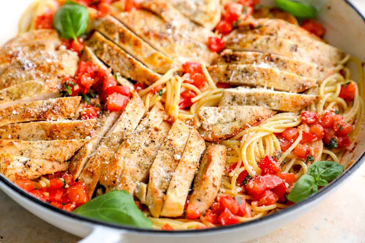 sliced chicken breasts over tomato bruschetta and angel hair pasta in a pan.