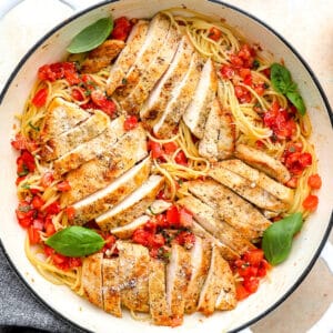 overhead view of bruschetta chicken pasta in a pan with basil leaves and fresh Parmesan.