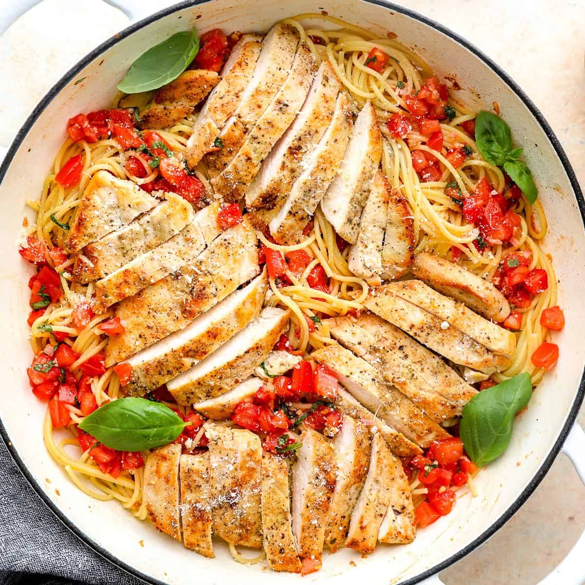 overhead view of bruschetta chicken pasta in a pan with basil leaves and fresh Parmesan.