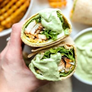 holding a halved chick fil a cool wrap dipped in avocado lime ranch dressing to show the filling.
