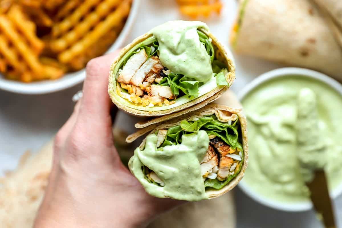 holding a halved chick fil a cool wrap dipped in avocado lime ranch dressing to show the filling.