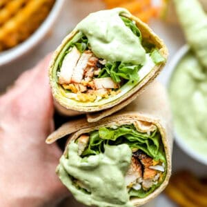 holding a halved chick fil a cool wrap dipped in avocado lime ranch dressing to show the filling.