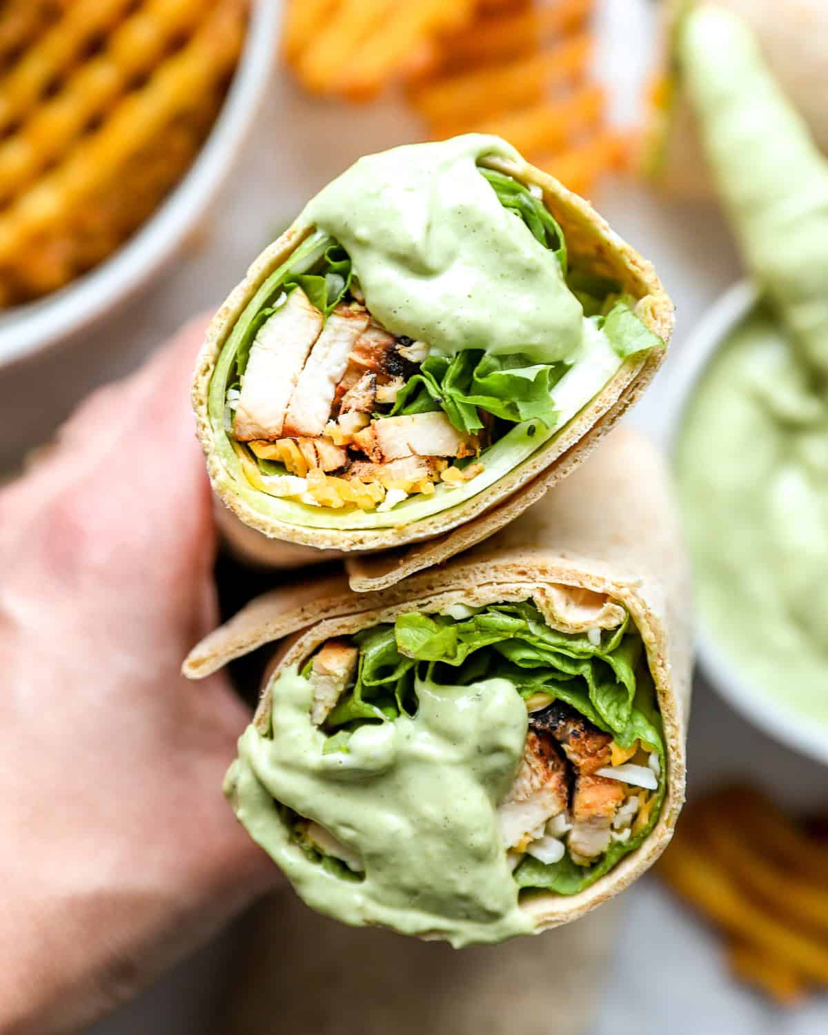holding a halved chick fil a cool wrap dipped in avocado lime ranch dressing to show the filling.