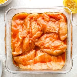 raw chicken breasts in marinade in a glass dish.