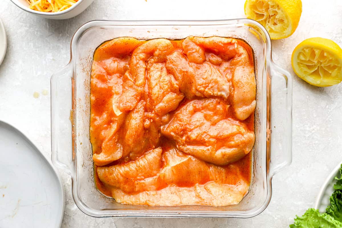 raw chicken breasts in marinade in a glass dish.
