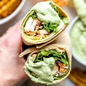 holding a halved chick fil a cool wrap dipped in avocado lime ranch dressing to show the filling.