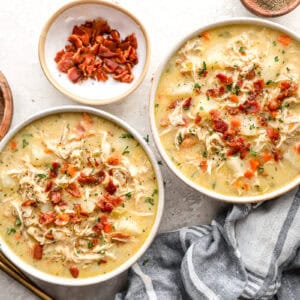 overhead view of two bowls of chicken and potato soup topped with bacon and parsley.