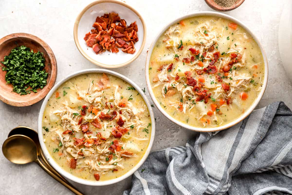 overhead view of two bowls of chicken and potato soup topped with bacon and parsley.