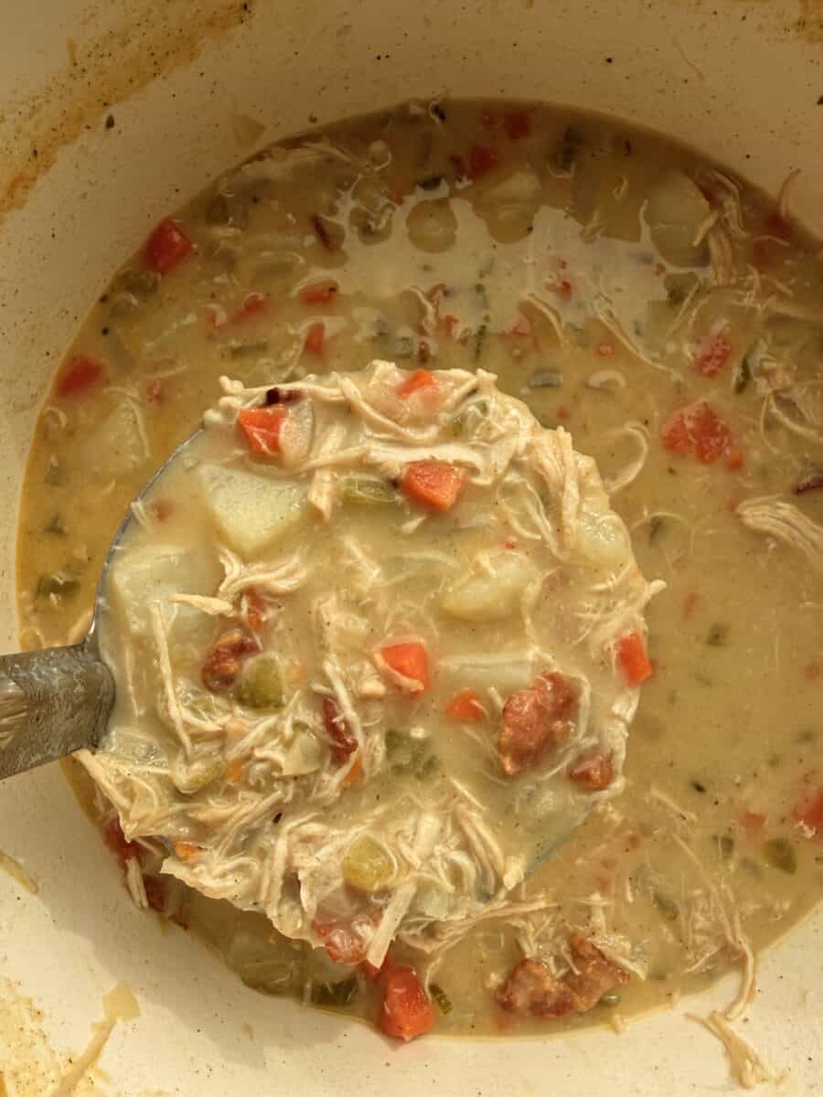 Ladling a portion of chicken potato soup out of a pot.