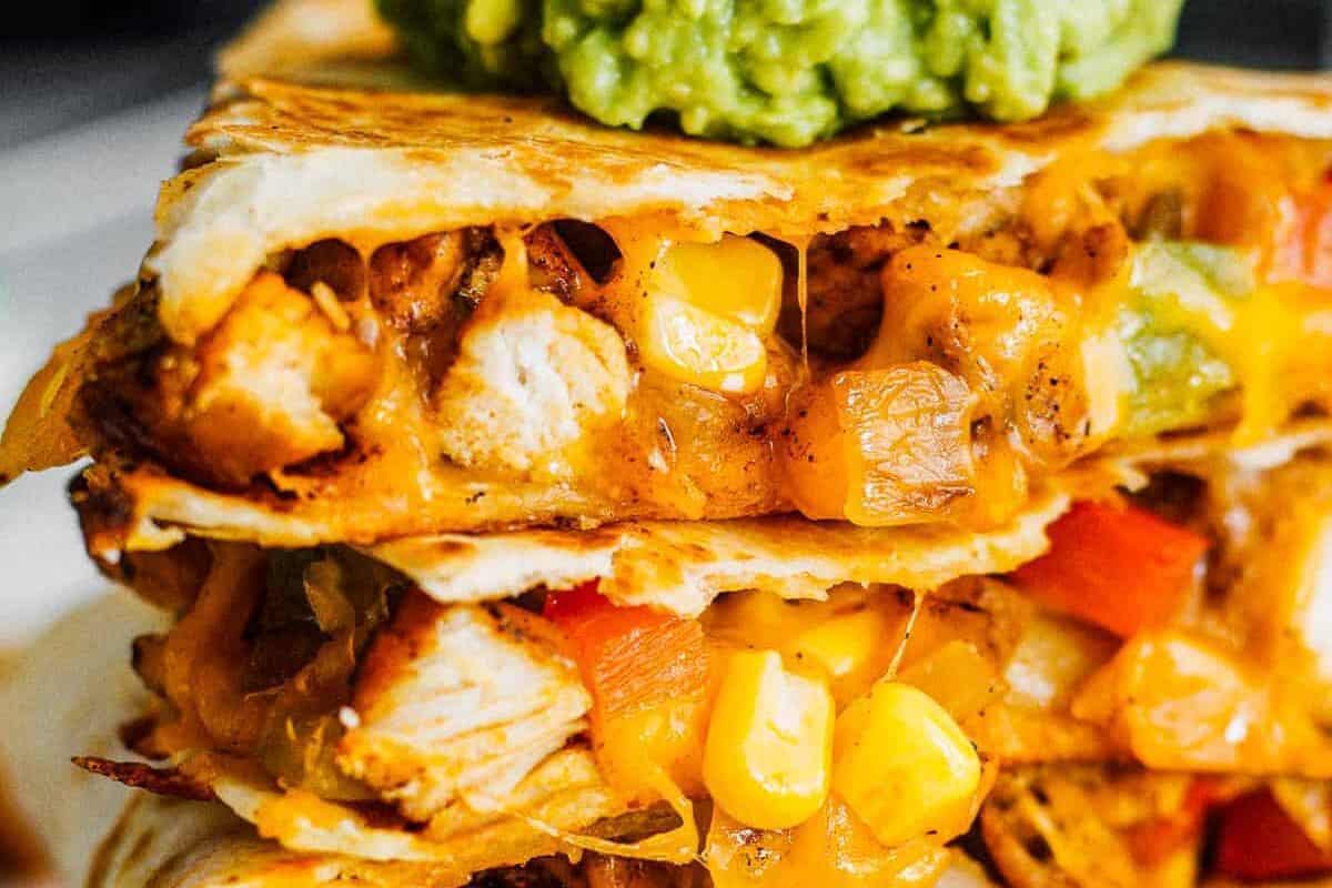 stacked triangles of chicken quesadillas loaded with veggies and cheese, topped with guacamole.