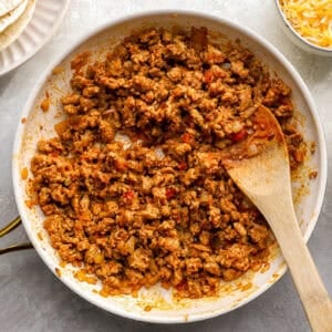 cooking seasoned ground chicken in a frying pan with a wooden spoon.