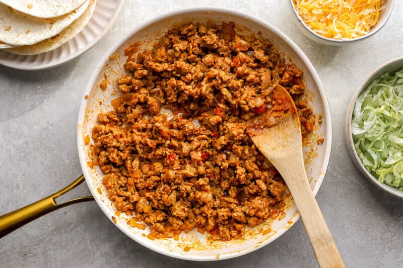 cooking seasoned ground chicken in a frying pan with a wooden spoon.