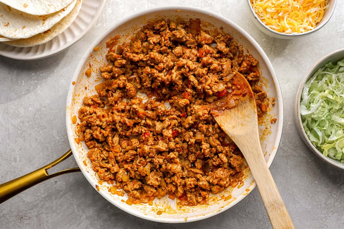 cooking seasoned ground chicken taco meat in a frying pan with a wooden spoon.