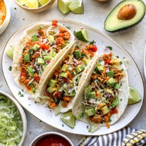 three ground chicken tacos on a platter surrounded by toppings.