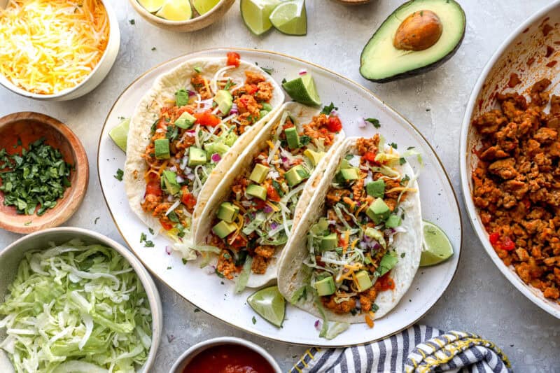 three ground chicken tacos on a platter surrounded by toppings.