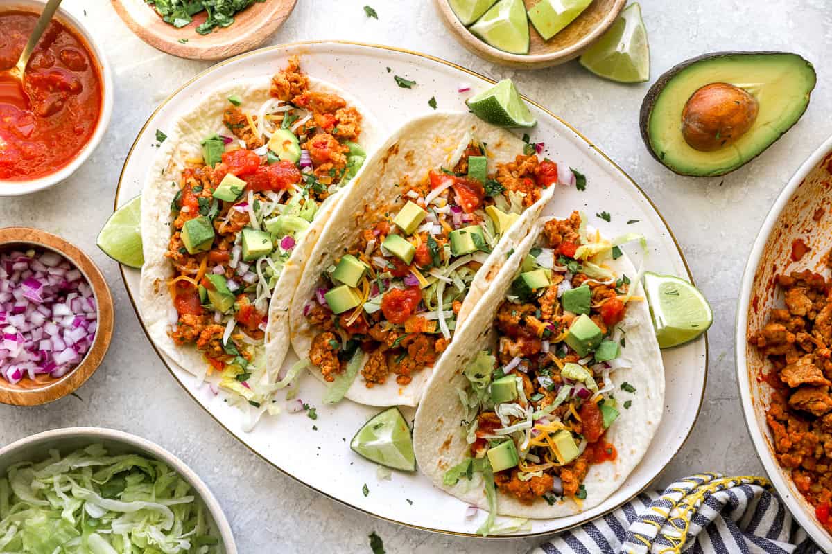 overhead view of 3 ground chicken tacos on a platter surrounded by toppings.