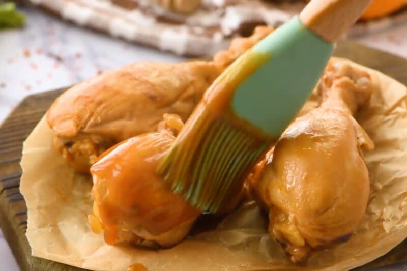 Brushing cooked chicken drumsticks with BBQ sauce.