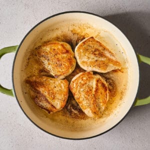 four seasoned seared chicken breasts in a skillet.