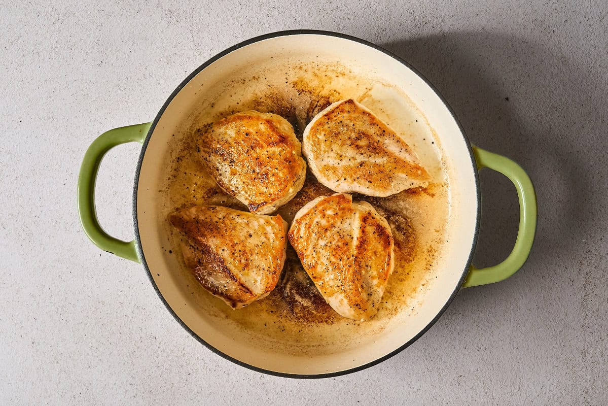 four seasoned seared chicken breasts in a skillet.