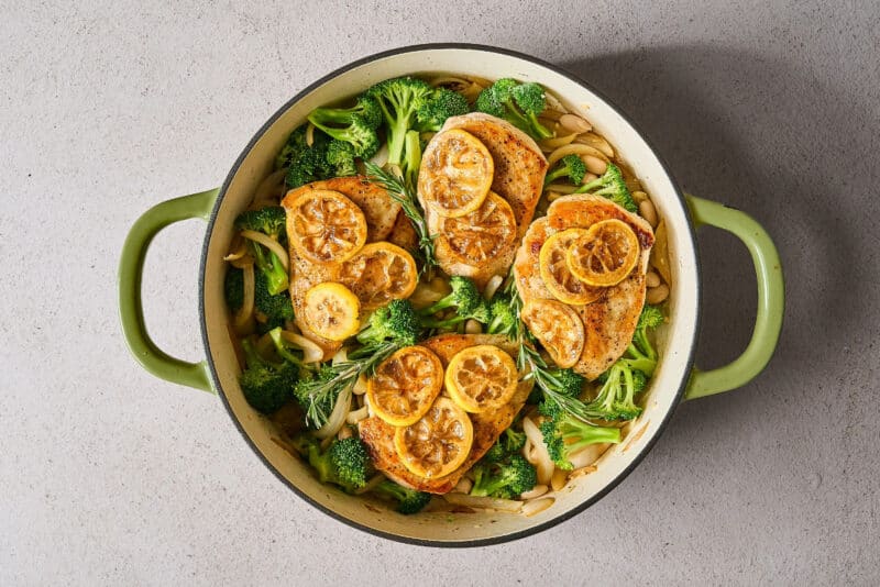chicken and lemon slices added to broccoli and white beans in a skillet.