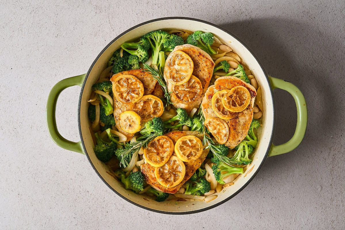 chicken and lemon slices added to broccoli and white beans in a skillet.