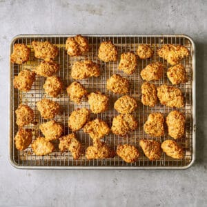 crispy bang bang chicken pieces on a wire rack set in a rimmed baking sheet, after baking a second time.