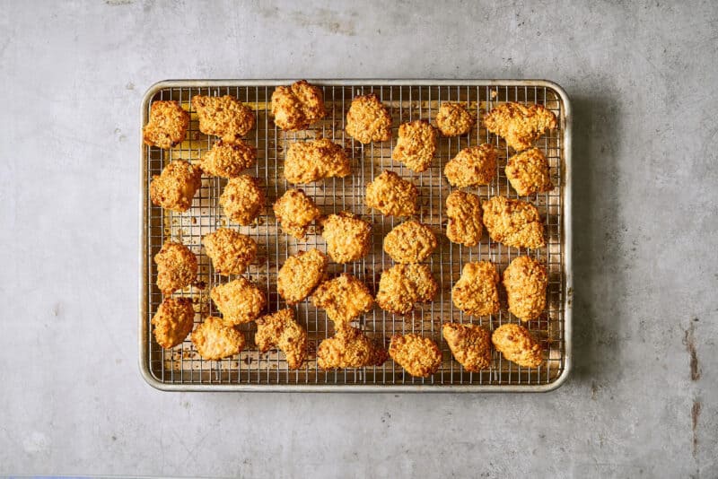 crispy bang bang chicken pieces on a wire rack set in a rimmed baking sheet, after baking a second time.