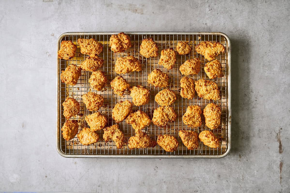 crispy bang bang chicken pieces on a wire rack set in a rimmed baking sheet, after baking a second time.