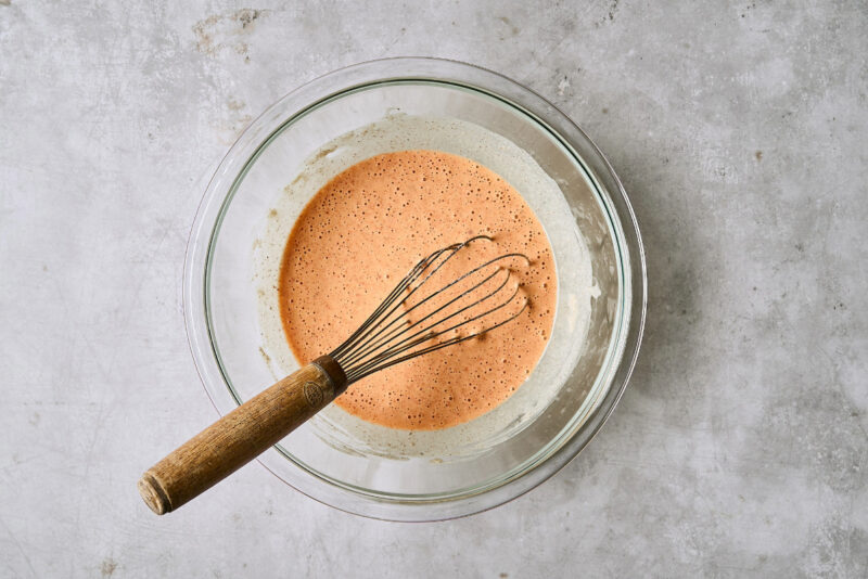 orange-colored batter in a glass bowl with a whisk.