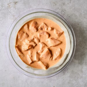 chicken pieces in orange-colored batter in a glass bowl.