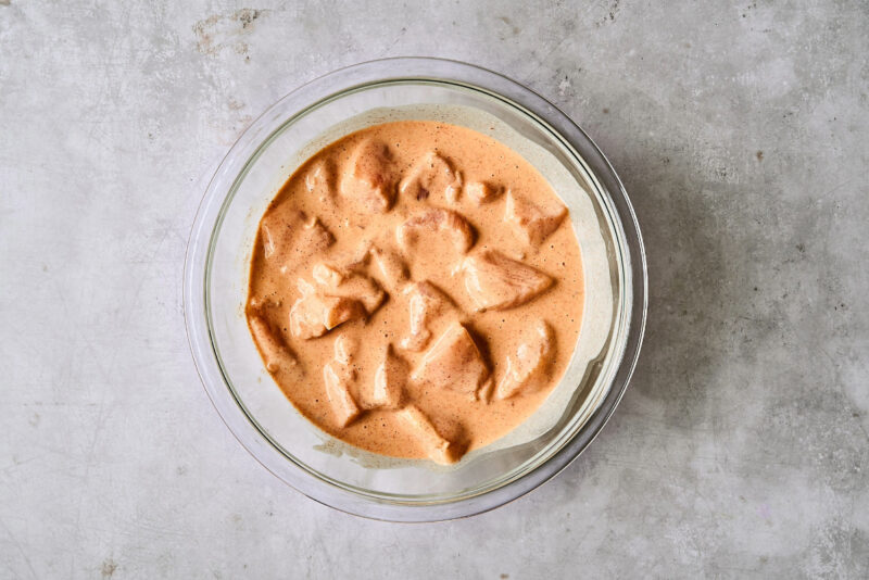 chicken pieces in orange-colored batter in a glass bowl.