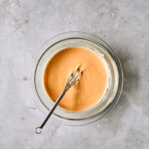 orange-colored bang bang sauce in a glass bowl with a whisk.