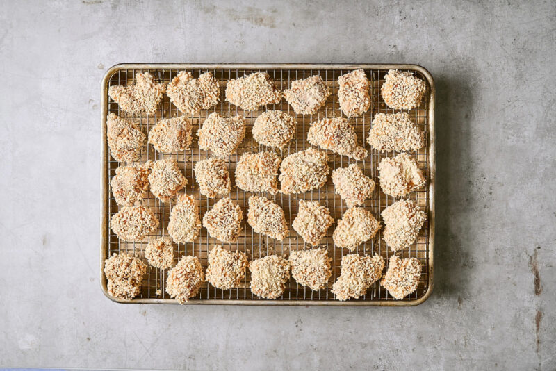 Panko-breaded chicken pieces on a wire rack set in a rimmed baking sheet.