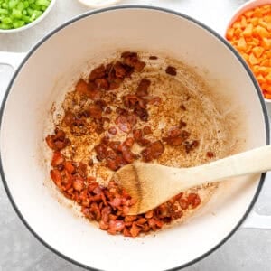frying bacon lardons in a dutch oven with a wooden spoon.