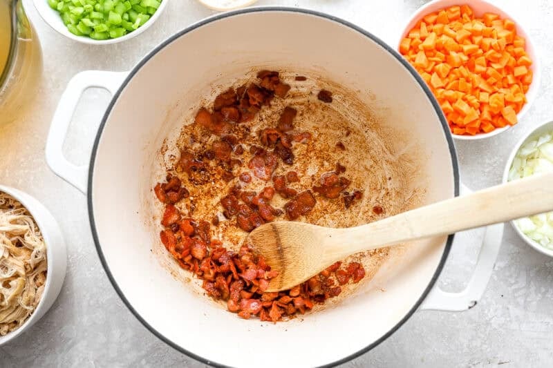 frying bacon lardons in a dutch oven with a wooden spoon.