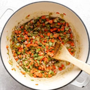 sautéeing vegetable mirepoix coated in flour in a dutch oven with a wooden spoon.