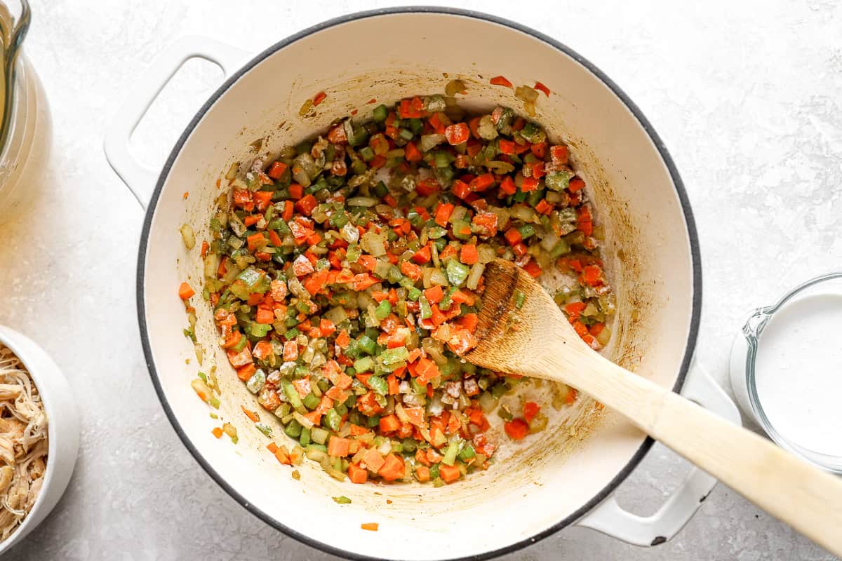 sautéeing vegetable mirepoix coated in flour in a dutch oven with a wooden spoon.
