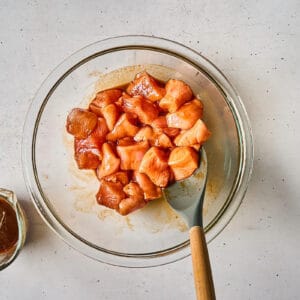 raw cubed chicken breast tossed in thick korean bbq sauce in a bowl.