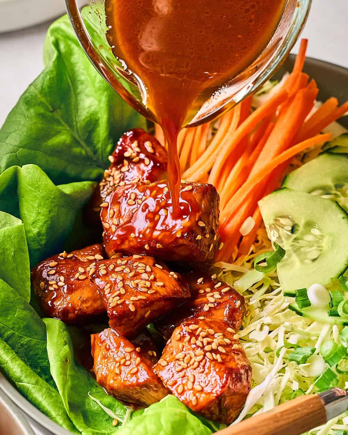 drizzling homemade Korean BBQ salad dressing over a fresh cabbage and butter lettuce salad with Gochujang chicken.